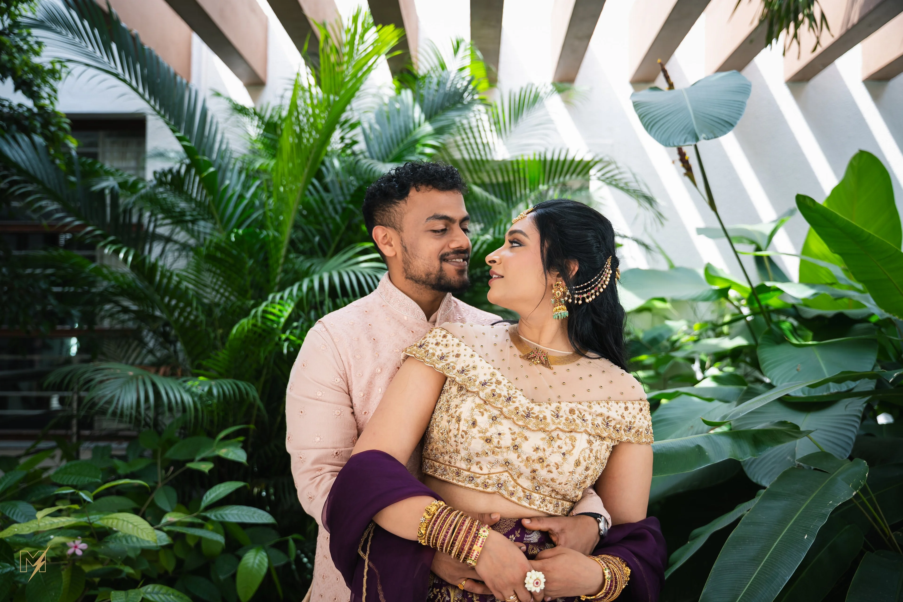 Romantic Couple Portrait Indian bride and groom sharing a romantic glance surrounded by lush green foliage.