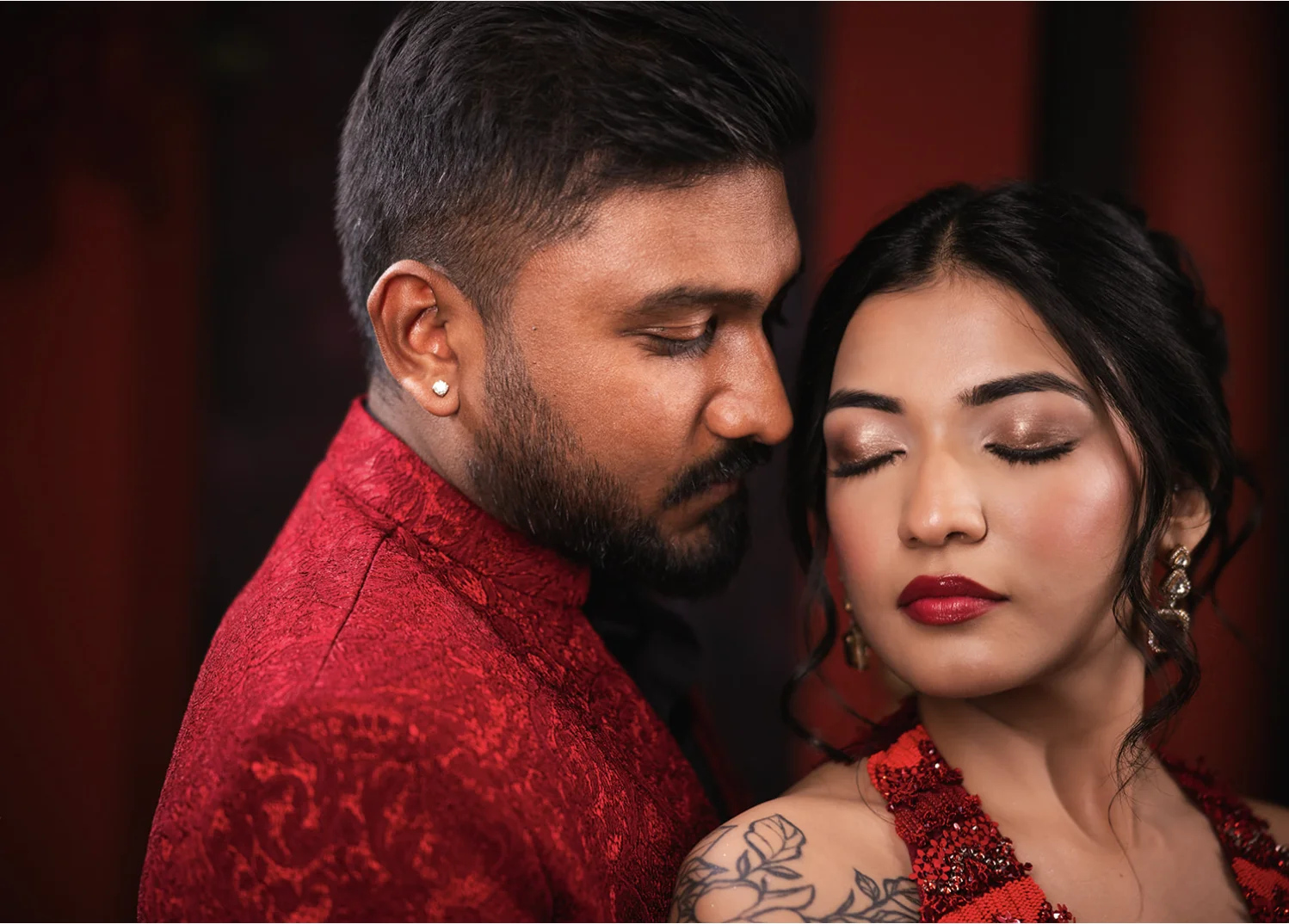 Close up of an Indian couple in matching red embroidered attire with eyes closed in an intimate moment.