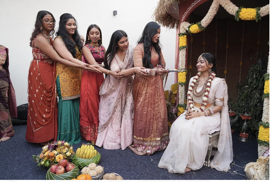 Indian bride in white saree receiving a festive ceremony blessing from her friends and family