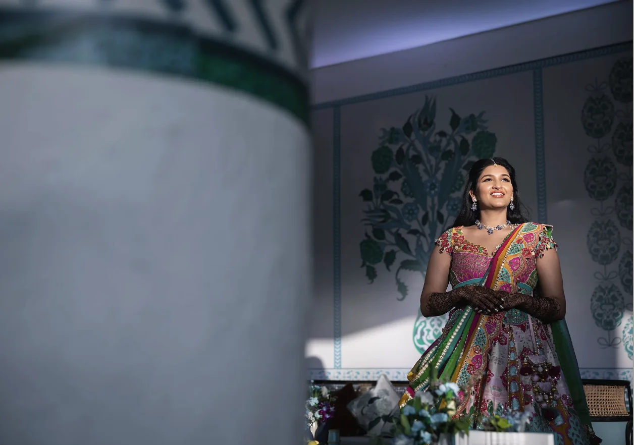 Indian bride in a colorful embellished lehenga smiling framed by classic architectural elements.