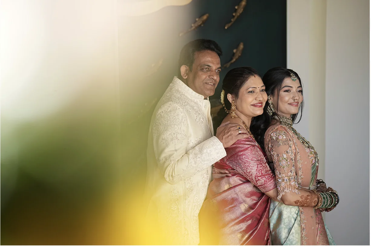 Indian bride posing with her parents in traditional wedding attire during a candid family moment.
