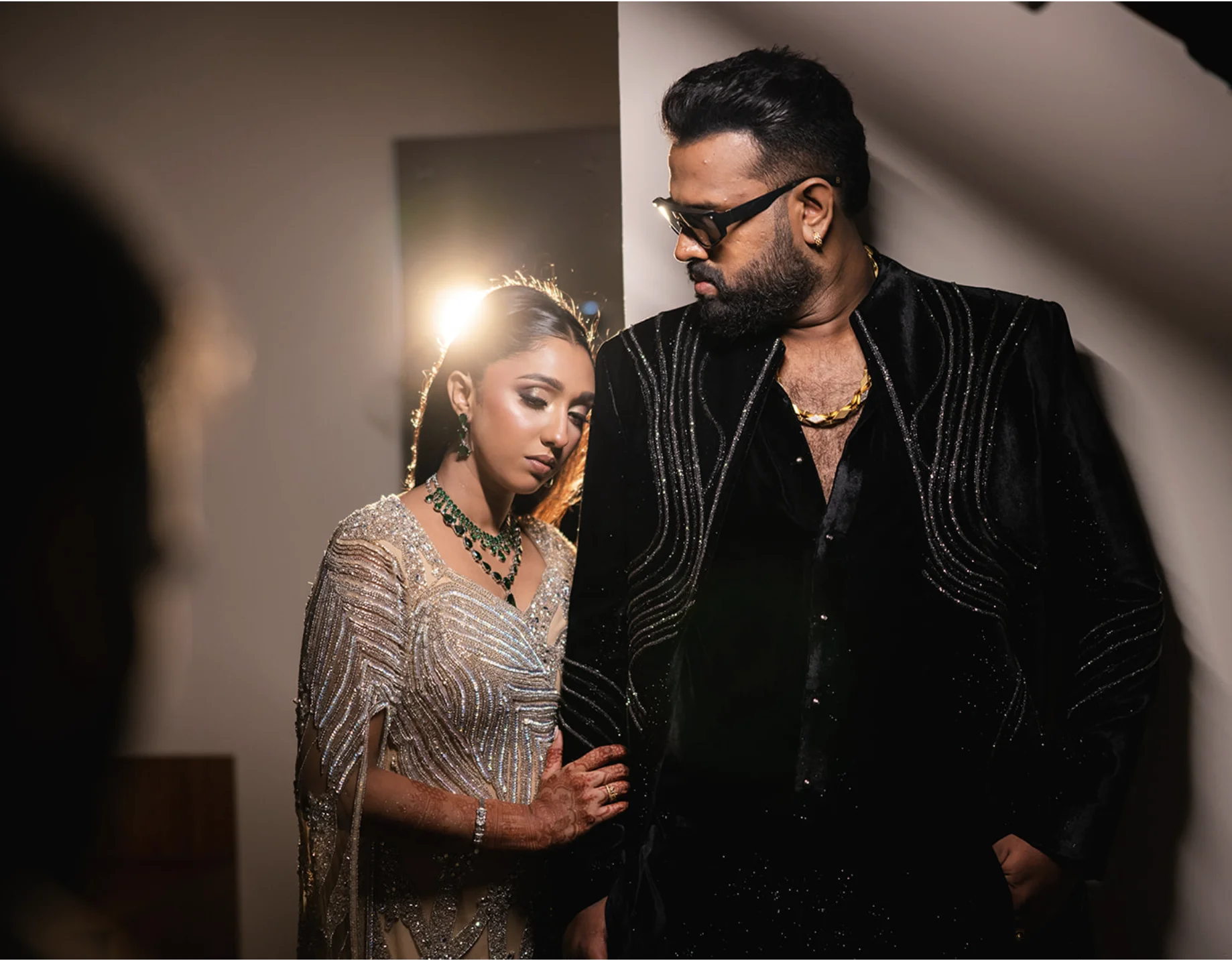 Indian couple posing in stylish evening reception wear under dramatic spotlighting.